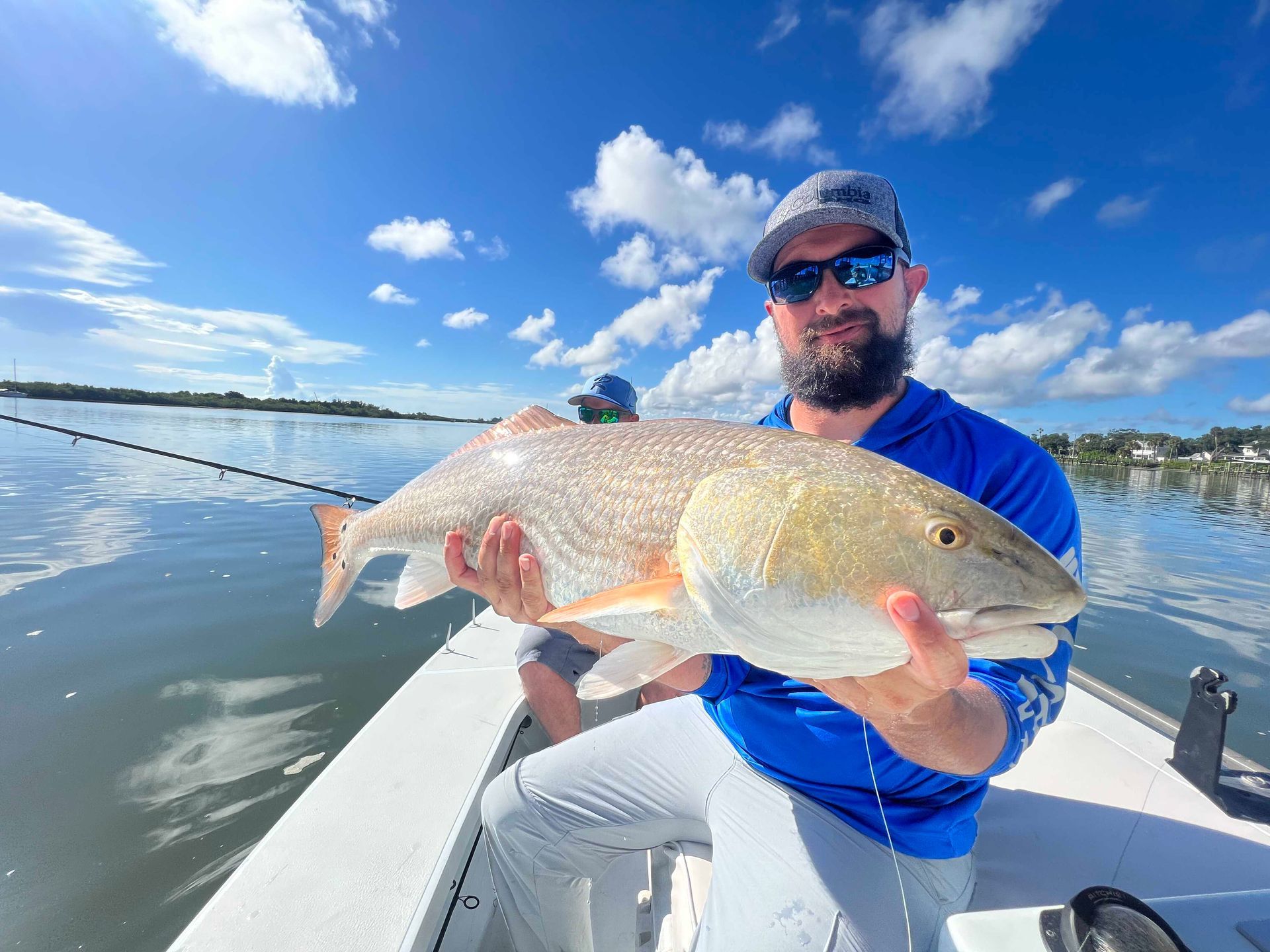 Man on a boat holding a large fish on a sunny lake under a blue sky