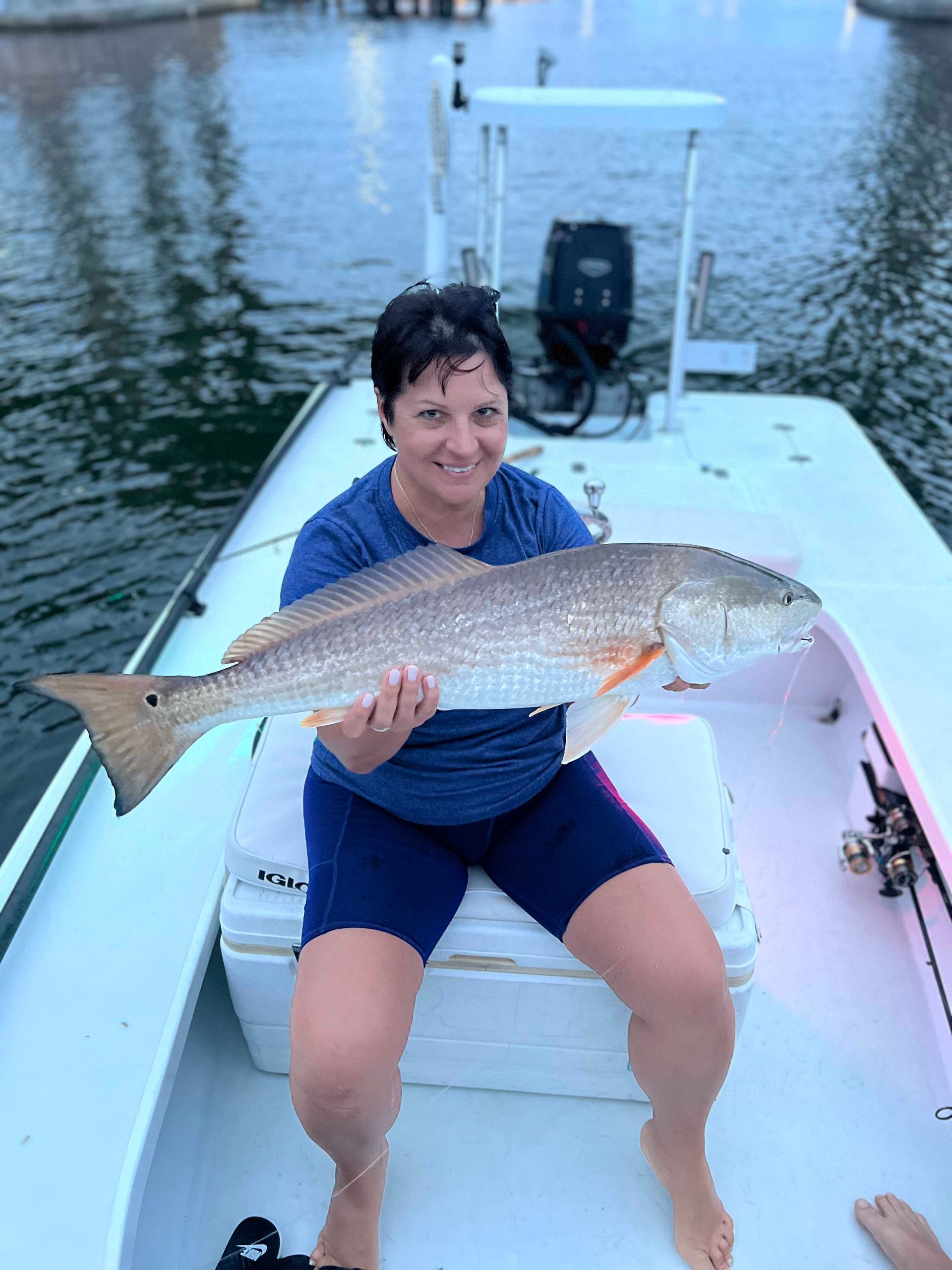 Person sitting on a boat holding a large fish, with calm water in the background.