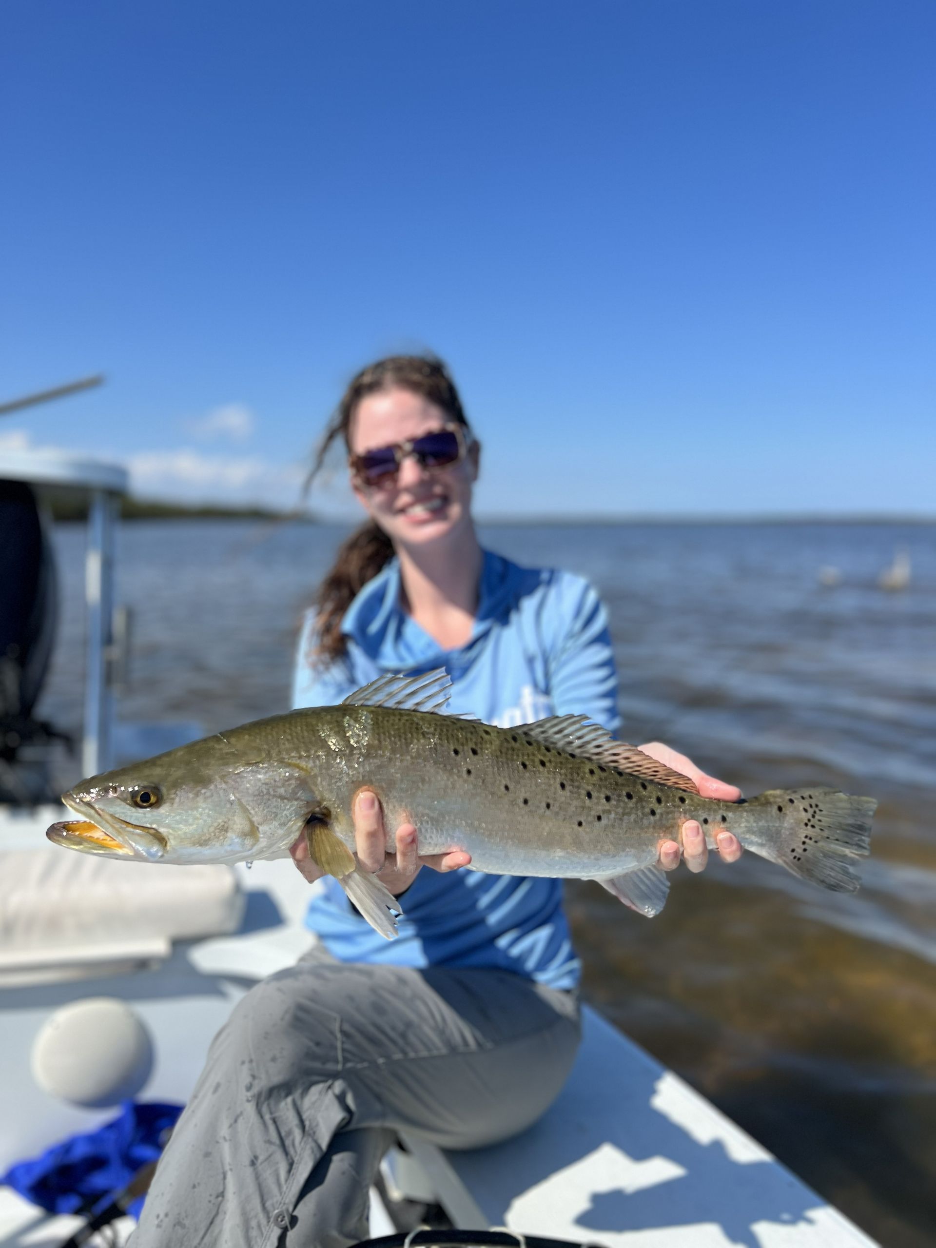Person on a boat holding a large fish on a sunny day with open water in the background