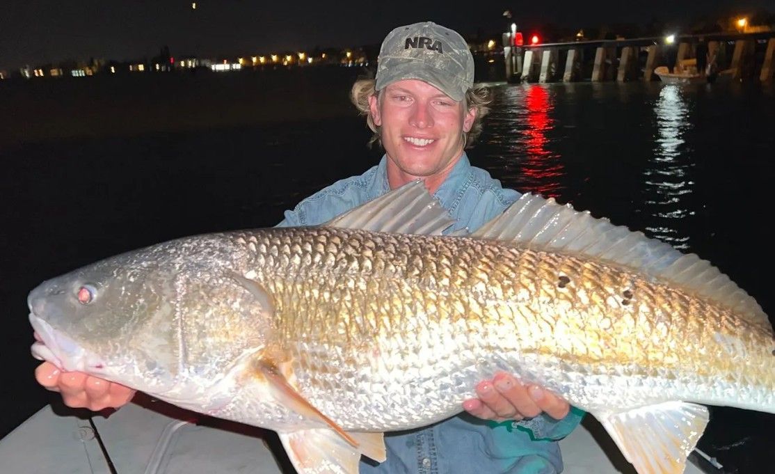 Person holding a large silver fish at night by the water