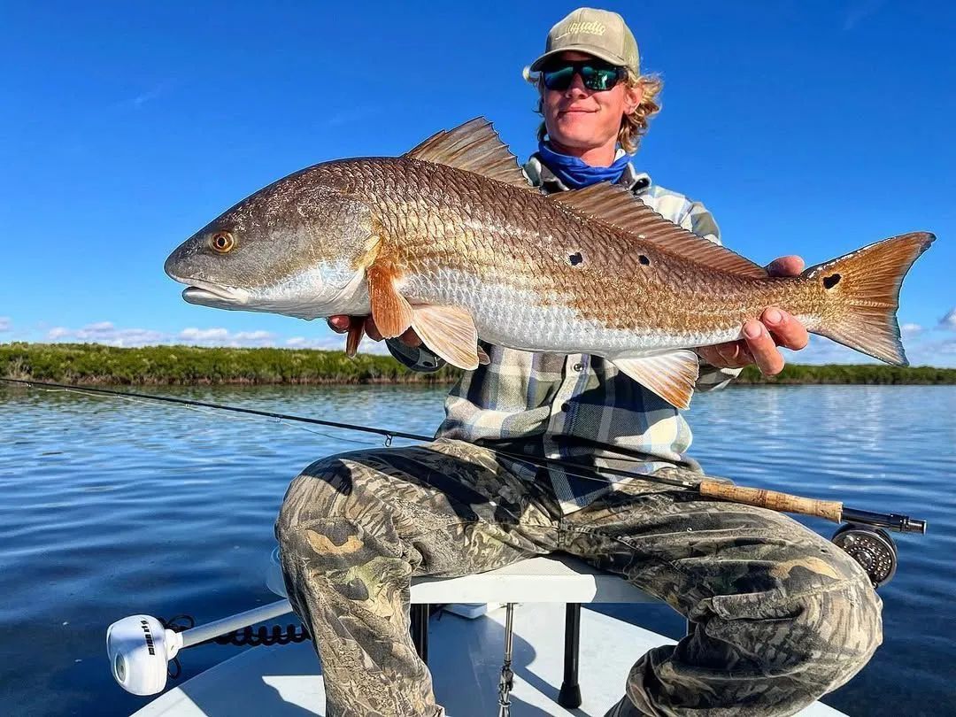 Angler holding a large fish on a boat against a bright blue sky and water background