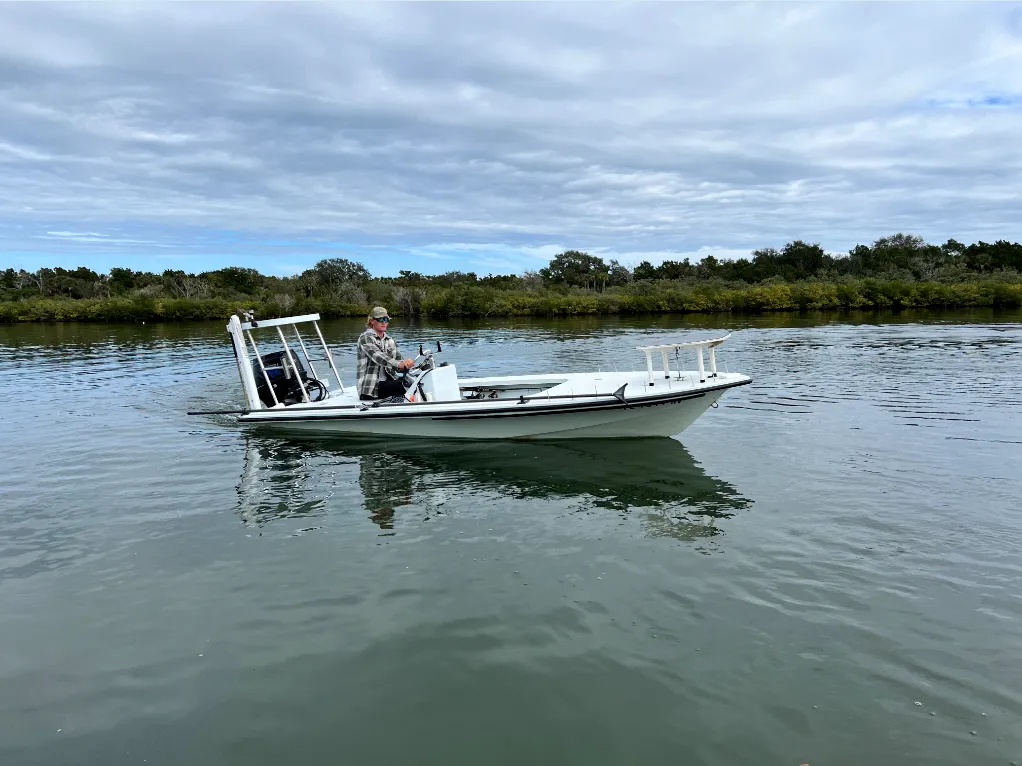 Small white boat on calm water near marshland under a cloudy sky