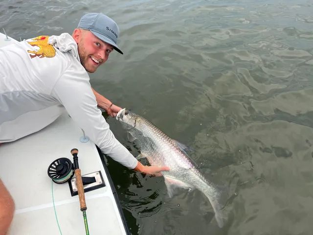 Angler on a boat holds a large fish in the water beside the boat