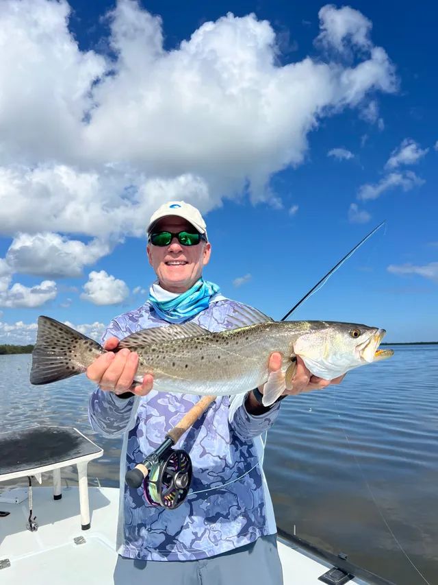 Angler holding a large fish on a boat under a bright blue sky