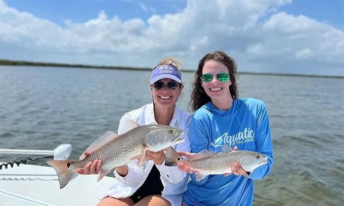 Two people on a boat holding large fish on a calm lake under a blue sky