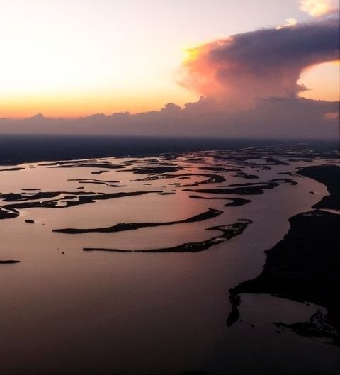 Sunset over winding water channels and marshland beneath a pink-orange sky