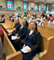Three women in black suits seated in a church pew, smiling and holding programs.