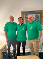 Three people in green shirts posing indoors in front of a framed painting.