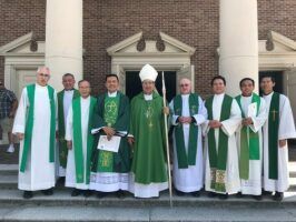 Group of clergy in green and white vestments standing in front of a brick building