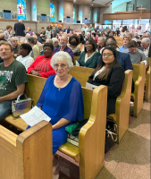 People seated in church pews, with a blue-dressed woman in the foreground and a congregation behind her.