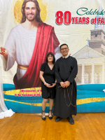 Two people posing in front of a large Jesus mural with “80 years” celebration text.