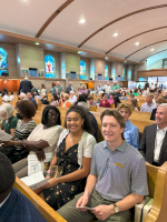 Audience seated in a church hall, smiling toward the camera during a large indoor event.