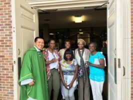 Group of people standing in a doorway, with one man in a green stole on the left.