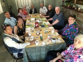 Group of people seated around a dining table in a living room, sharing a meal and smiling.