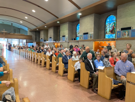 Congregation seated in church pews during a service, with stained-glass windows and arched ceiling.