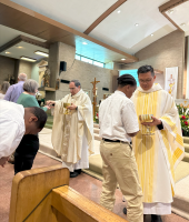Priests in white and gold vestments greet people inside a church during a religious service