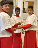 Three children in red-and-white costumes hold a sword together in a hallway