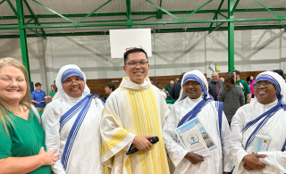 Group of people in white and yellow religious robes posing in a hall, one holding a book