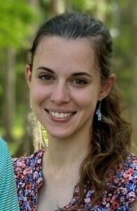 Smiling person outdoors with a floral top and earrings, standing against a blurred green background