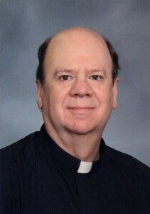 Portrait of a smiling clergyman in a black shirt with a white clerical collar against a gray background