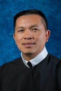 Portrait of a person in a black collared robe against a blue studio background.