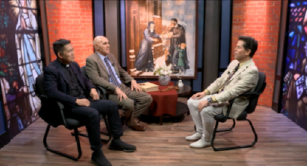 Three men seated in a studio interview set with a portrait painting in the background