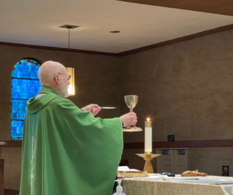 Priest in green vestments elevates a chalice during Mass beside an altar and lit candle