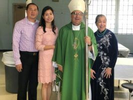 Four people posing indoors, including a man in green ceremonial vestments holding a staff.