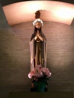 Statue of a robed figure with flowers, set against a brick wall under a curved lighted alcove