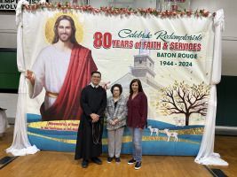 Three people posing before a colorful 80th anniversary church event backdrop in Baton Rouge.