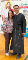 Two people posing indoors in front of a “Celebrating 25 Years of Faith” poster