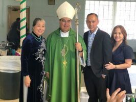 Four people posing indoors, including a bishop in green vestments and mitre, with two others beside him.
