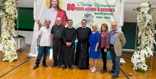 Group posing in front of an 80th anniversary banner at a celebratory event with floral displays
