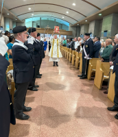 Ceremony inside a church aisle with clergy in white and gold robes and attendees seated on both sides