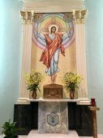Religious altar with a painted Christ figure, flanked by flowers and candles on a marble pedestal