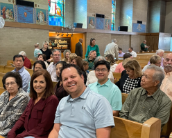 Congregation seated in wooden pews inside a church, with people smiling toward the camera.