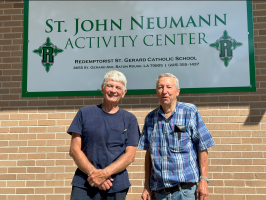 Two men standing in front of the St. John Neumann Activity Center sign.