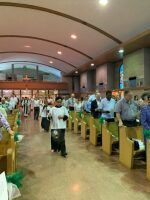 People standing in church pews during a service inside a bright arched sanctuary