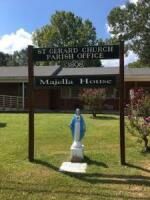 St. Gerard Church parish office sign with a small blue Virgin Mary statue in front on a sunny lawn