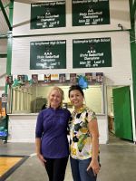 Two people smiling in a school hallway with green signs overhead