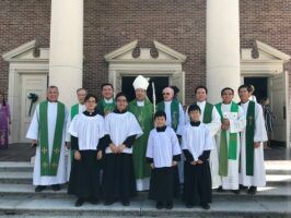 Group of clergy in white and green robes standing on church steps