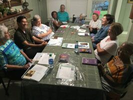 Group of people seated around a table in a meeting room, discussing papers and books.