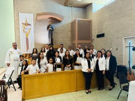 Group posing in a church sanctuary with a statue and altar, many wearing white tops and black pants.