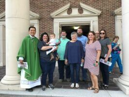 Group posing on church steps with a green-robed priest beside a white column