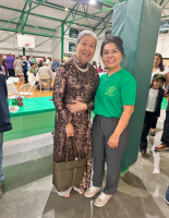 Two women smiling and posing together at an indoor event, one in a dark dress and one in a green shirt.