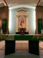 Church altar with green cloth, central religious banner, and candles beneath an arched alcove