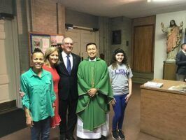 Five people posing indoors, including a man in green clergy robes, in a church-like room