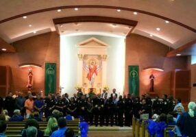 Congregation gathered in a church sanctuary before an altar with a religious mural and statues.