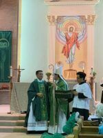 Clergy in green vestments celebrate Mass at an altar in a church with a religious mural backdrop