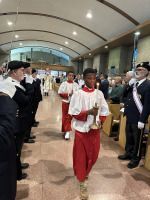Procession in an arched hallway, with a person in red and white leading people in black-and-white uniforms